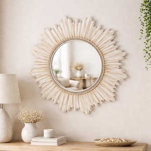 Peut inclure: Un miroir mural rond doté d'un cadre en forme de soleil avec une finition blanc cassé vieillie. Le centre en verre circulaire est entouré d'une bordure intérieure perlée et de rayons en bois rayonnants de longueurs variées.
