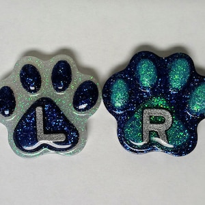 May include: Two glitter paw print charms, one blue and white with the letter "L" and one teal and blue with the letter "R".