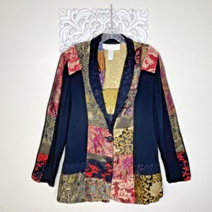 May include: A long-sleeve blazer featuring a patchwork design with solid black panels and various patterned fabric sections in gold, red, and purple tones. The garment has a shawl collar, a three-button front closure, and a white interior brand label.