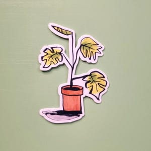 Peut inclure: Un autocollant représentant une illustration d'une plante en pot. La plante a des feuilles jaunes et un pot marron. L'autocollant est sur un fond vert clair.