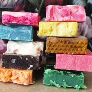 May include: A stack of nine colourful handmade soap bars. The bars are arranged in a pyramid shape, with the largest bar at the bottom and the smallest bar at the top. The bars are made with natural ingredients and have a variety of scents and colours.
