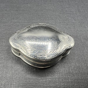 May include: A silver, ornate, decorative box with a hinged lid. The box has a wavy, organic design.