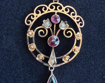 May include: Gold-toned pendant with a circular design, featuring a central round gemstone and a teardrop-shaped gemstone. The pendant is adorned with smaller gemstones and floral accents, showcasing an ornate and vintage aesthetic.