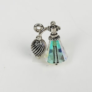 Puede incluir: Un dije de botella de perfume en miniatura con un acabado metálico plateado. La botella presenta un bulbo acanalado en forma de pera y una base de cristal iridiscente facetada. El diseño incluye una boquilla curva y detalles decorativos.