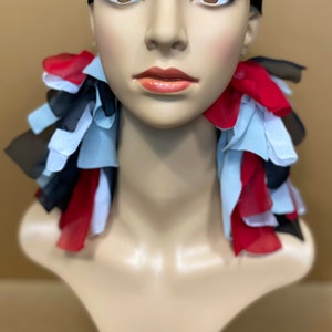 May include: A mannequin head with black hair and red, white, and black fabric tied around the neck. The fabric is in a ruffled style.