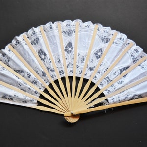 May include: A white lace hand fan with a wooden frame. The fan is closed and has a delicate lace pattern.