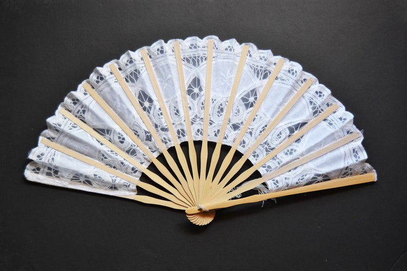 May include: A white lace hand fan with a wooden frame. The fan is closed and has a delicate lace pattern.