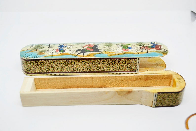Puede incluir: Una caja de madera con una tapa con bisagras. La tapa est&aacute; decorada con una escena colorida de personas montando a caballo. La caja est&aacute; hecha de madera y tiene un patr&oacute;n decorativo en los lados.