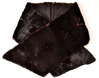 Peut inclure: Une écharpe en fourrure marron foncé avec une doublure noire. L'écharpe est faite d'une matière douce et texturée et est conçue pour être portée autour du cou. L'écharpe est un accessoire luxueux.