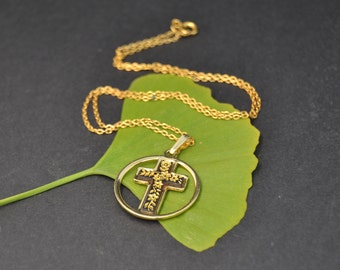 May include: A gold chain necklace with a pendant featuring a black cross with gold floral details. The pendant is surrounded by a gold circle.