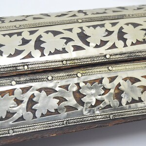 May include: A wooden box with intricate silver floral designs and decorative metal accents. The box is closed and the top is visible.