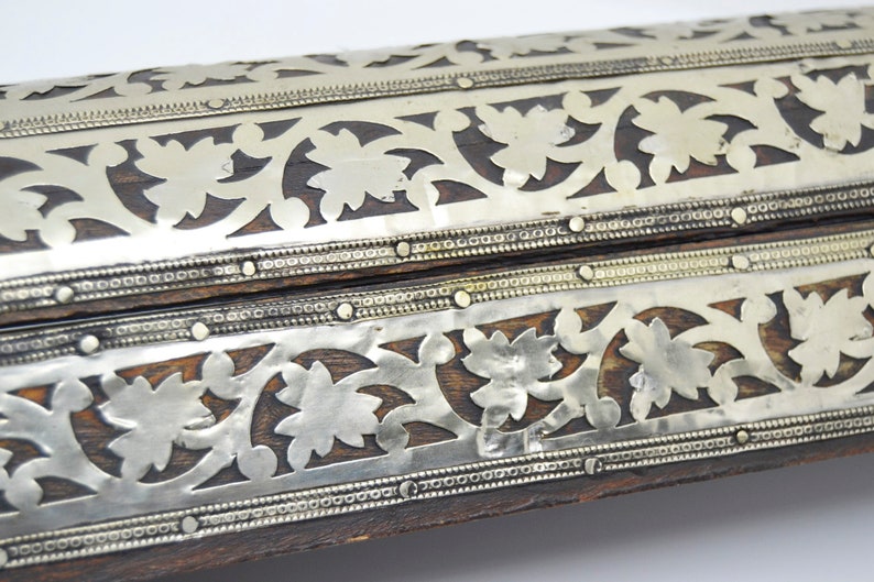 May include: A wooden box with intricate silver floral designs and decorative metal accents. The box is closed and the top is visible.