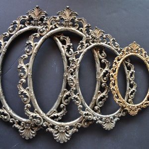 May include: Four ornate oval picture frames, three silver and one gold, with intricate floral designs. The frames are nested together, with the largest frame in the back and the smallest frame in the front.