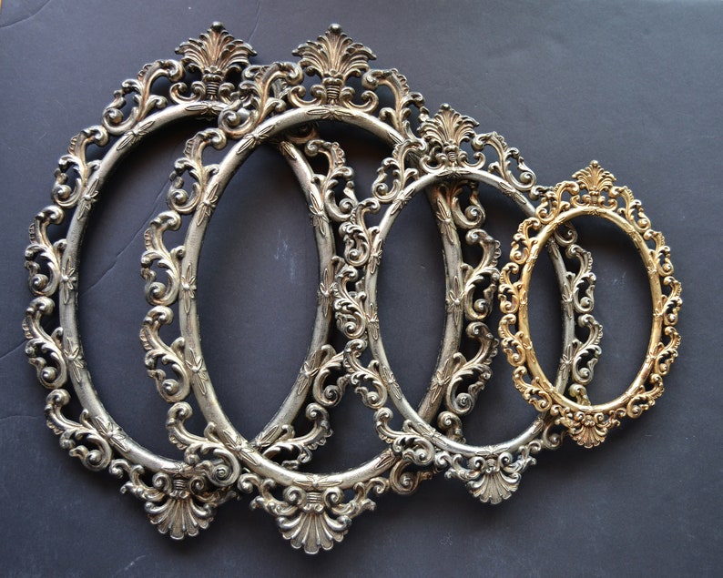 May include: Four ornate oval picture frames, three silver and one gold, with intricate floral designs. The frames are nested together, with the largest frame in the back and the smallest frame in the front.