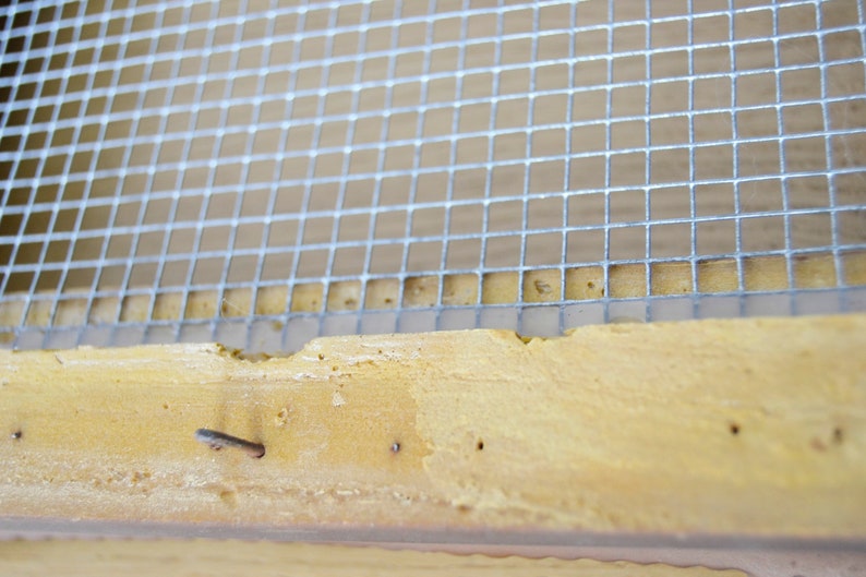 May include: Close-up of a wooden frame with a silver wire mesh screen attached. The screen is secured with nails.