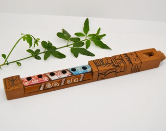Puede incluir: Una flauta de madera con un diseño tallado y detalles pintados. La flauta tiene seis agujeros y está decorada con pintura roja, azul y blanca. La flauta mide aproximadamente 30 cm de largo.