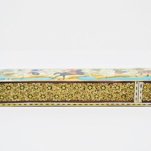 Puede incluir: Una caja larga y rectangular con un dise&ntilde;o colorido e intrincado. La caja est&aacute; hecha de madera y tiene una tapa con bisagras. La parte superior de la caja presenta una escena de personas montando a caballo, con un fondo azul y blanco. La parte inferior de la caja tiene un patr&oacute;n repetitivo de flores y formas geom&eacute;tricas.