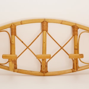 May include: A wall-mounted coat rack made of natural bamboo with three hooks. The rack has a curved top and a woven design.