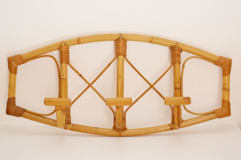 May include: A wall-mounted coat rack made of natural bamboo with three hooks. The rack has a curved top and a woven design.