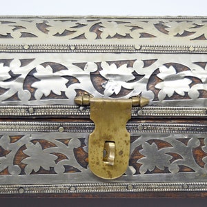 May include: A wooden box with a silver and brass inlay design. The box has a brass latch and hinges.