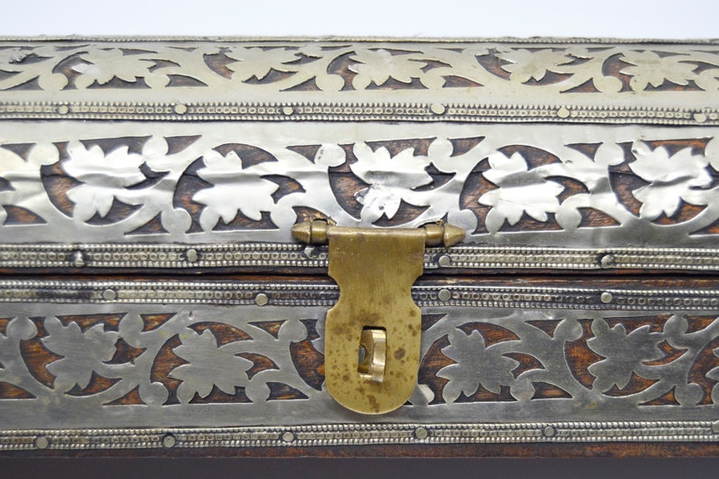 May include: A wooden box with a silver and brass inlay design. The box has a brass latch and hinges.