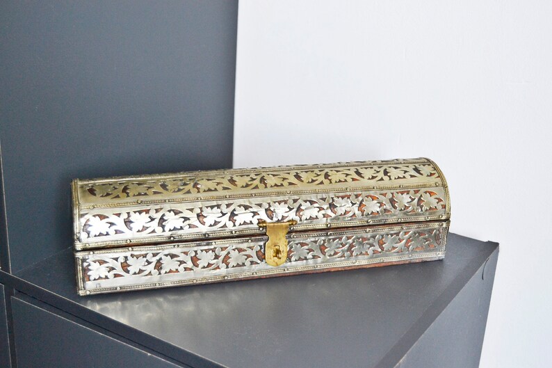 May include: A silver and gold decorative box with intricate floral patterns. The box has a hinged lid and a brass clasp.