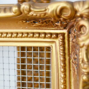 May include: An ornate picture frame in a gold colour with a wire mesh insert. The frame has a decorative, ornate design.