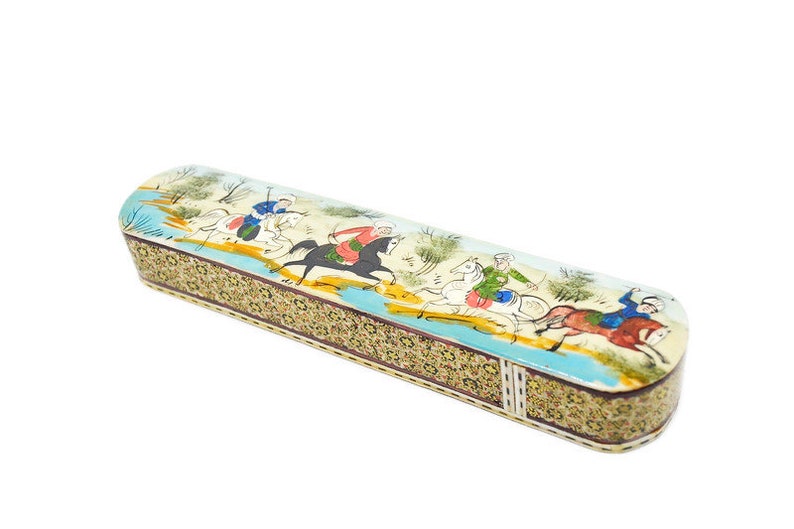 Puede incluir: Una caja larga y rectangular con un dise&ntilde;o colorido pintado a mano que representa a personas montando a caballo. La caja est&aacute; hecha de madera y tiene un patr&oacute;n decorativo intrincado alrededor de los bordes.