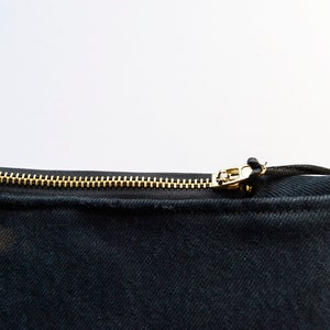 May include: A black canvas zippered pouch with a gold zipper and a black drawstring. The pouch has a brown and black tie-dye pattern on one side.