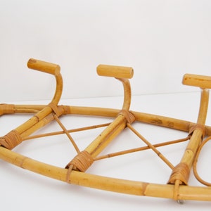 May include: A natural bamboo coat rack with three hooks. The rack is made of woven bamboo and has a curved shape.