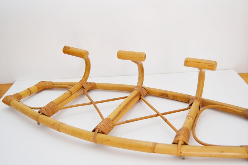 May include: A natural bamboo coat rack with three hooks. The rack is made of woven bamboo and has a curved shape.