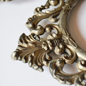 May include: A silver-toned ornate picture frame with a detailed, intricate design. The frame is made of metal and has a vintage look.