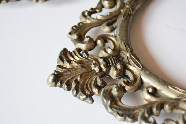 May include: A silver-toned ornate picture frame with a detailed, intricate design. The frame is made of metal and has a vintage look.
