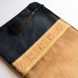 May include: A black and brown fabric pouch with a tassel. The pouch has a decorative trim with pink and white squares.
