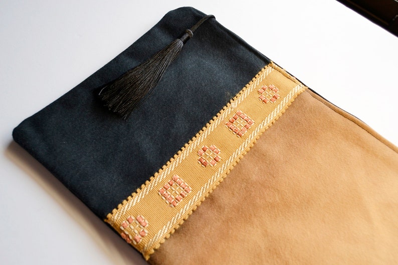May include: A black and brown fabric pouch with a tassel. The pouch has a decorative trim with pink and white squares.