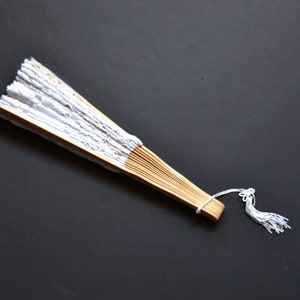 May include: A white lace folding fan with a wooden handle and a white tassel.
