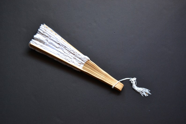 May include: A white lace folding fan with a wooden handle and a white tassel.