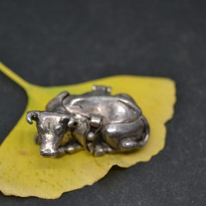 May include: A silver cow figurine with a detailed design, resting on a yellow ginkgo leaf.
