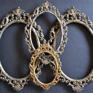 May include: Three ornate silver oval picture frames with a smaller gold oval frame in the center.