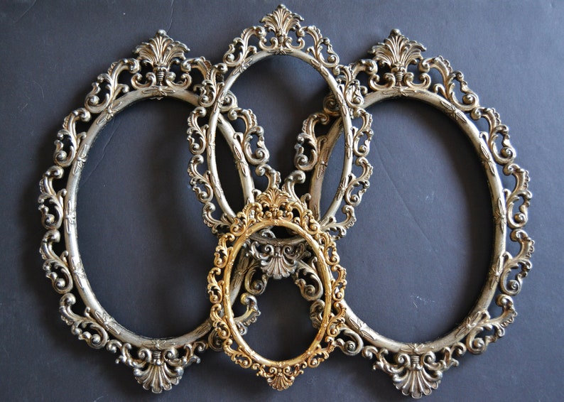 May include: Three ornate silver oval picture frames with a smaller gold oval frame in the center.
