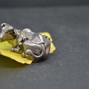May include: A silver figurine of a cow lying down on a yellow leaf. The cow is detailed with intricate carvings and has a realistic appearance.