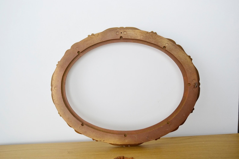 May include: A gold oval picture frame with a decorative, ornate design. The frame is made of wood and has a smooth finish.