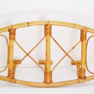 May include: A wall-mounted bamboo coat rack with a curved top and three hooks. The rack is made of natural bamboo and has a woven design.