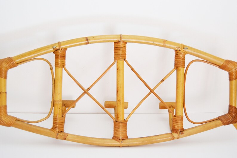 May include: A wall-mounted bamboo coat rack with a curved top and three hooks. The rack is made of natural bamboo and has a woven design.