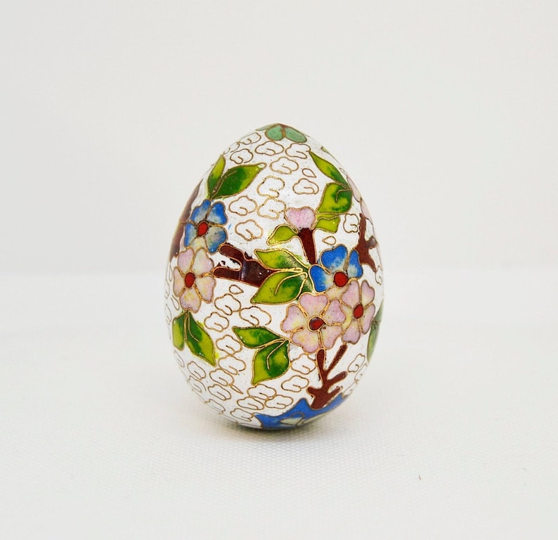 May include: A white egg-shaped decorative object with a floral design. The design features pink, blue, and red flowers with green leaves and gold accents.