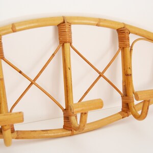 May include: A natural bamboo coat rack with a curved top and three hooks. The rack is made of woven bamboo and has a natural finish.