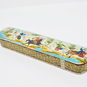 Puede incluir: Una caja de madera rectangular con una escena pintada colorida de personas montando a caballo. La caja est&aacute; decorada con intrincados patrones de mosaico en tonos dorados, marrones y blancos.