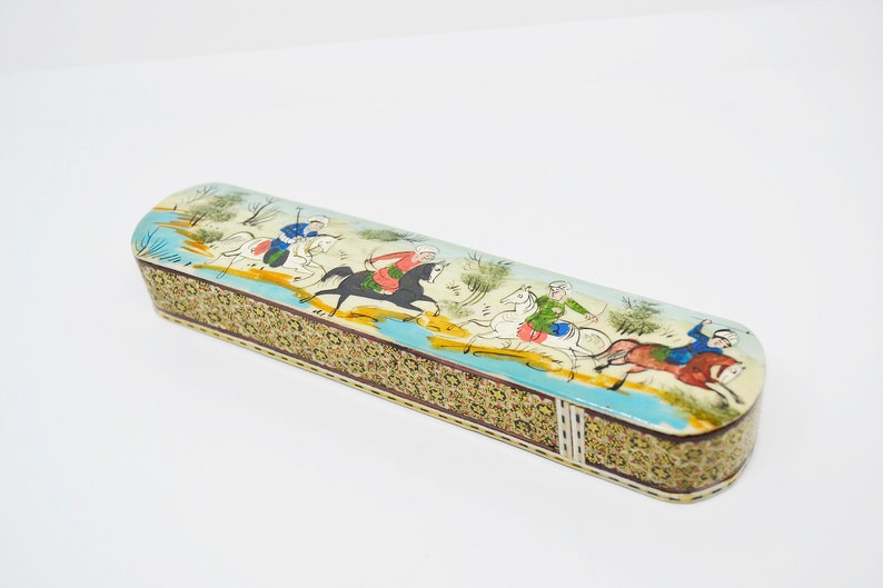 Puede incluir: Una caja de madera rectangular con una escena pintada colorida de personas montando a caballo. La caja est&aacute; decorada con intrincados patrones de mosaico en tonos dorados, marrones y blancos.