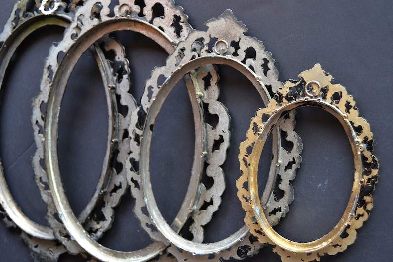 May include: Four oval-shaped picture frames with ornate, silver-colored metal frames. The frames are nested together, with the smallest frame in the front and the largest frame in the back.