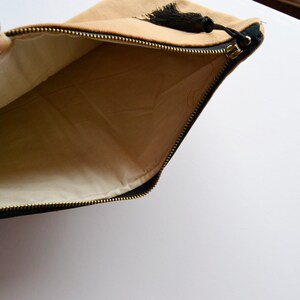 May include: A tan and black zippered pouch with a black tassel. The pouch is open and the inside is lined with a cream-colored fabric.